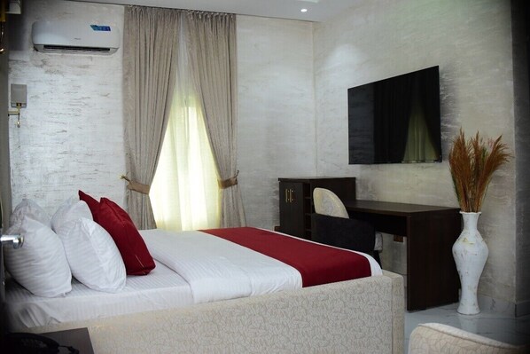 A hotel room with a bed, a desk, a chair, a vase, and a mounted TV.