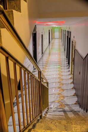 A hallway with a marble floor, a staircase with a golden railing, and doors on either side.