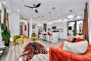 Ein modernes Wohnzimmer mit einer Couch, Sesseln, einem Teppich und einer Küche im Hintergrund.