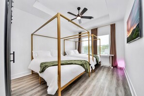 Ein modernes Schlafzimmer mit einem Himmelbett, einem Deckenventilator und einem großen Fenster mit Vorhängen.