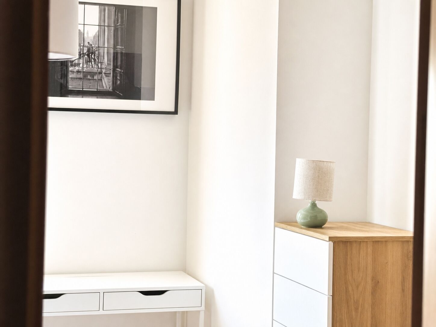 Une pièce au décor minimaliste, avec un bureau blanc, une armoire en bois et un tableau encadré accroché au mur.