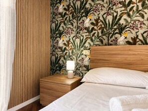 Ein Hotelzimmer mit einem hölzernen Kopfteil, einem Nachttisch mit Lampe und floralem Wandpapier.