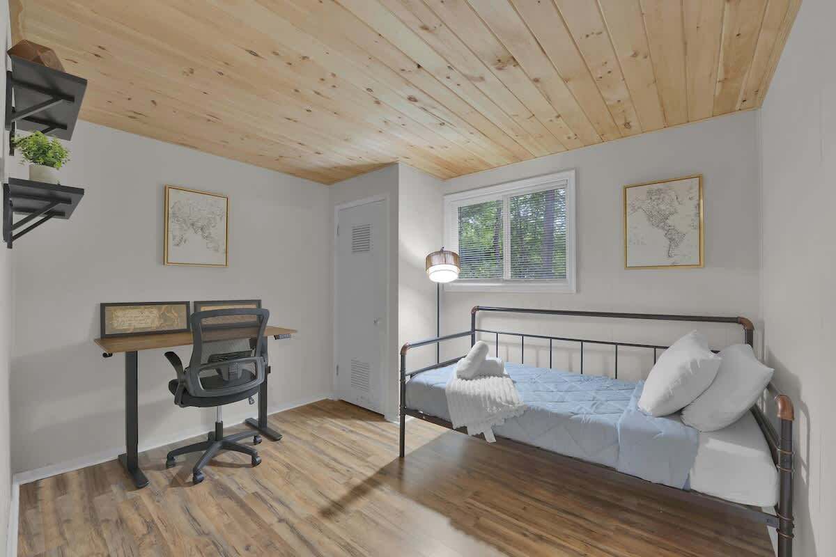 Een slaapkamer met een houten plafond, een bed met wit beddengoed, een bureau met stoel, en twee wandlampen.