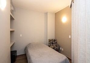 A small, neatly arranged bedroom with a single bed, a chair, and a shelf. - SHB Oásis Familiar Pé na Areia (Santos)