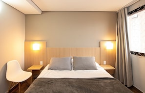 A hotel room with a bed, two bedside lamps, a chair, and a window with curtains. - SHB Oásis Familiar Pé na Areia (Santos)