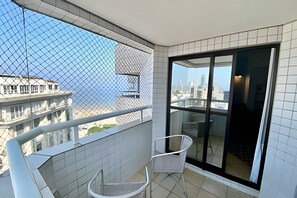 A balcony with a view of buildings, a chair, and a glass door. - SHB Oásis Familiar Pé na Areia (Santos)
