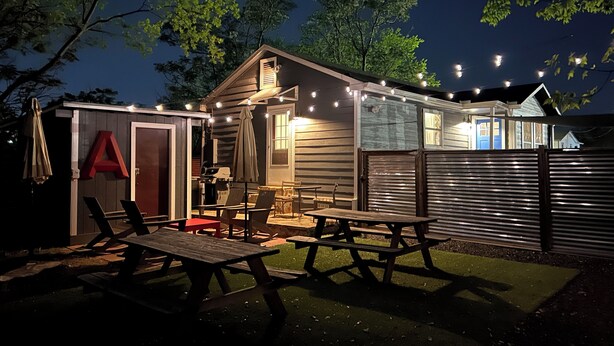 Een kleine blokhut met een terras, buitenmeubels en sfeerverlichting.