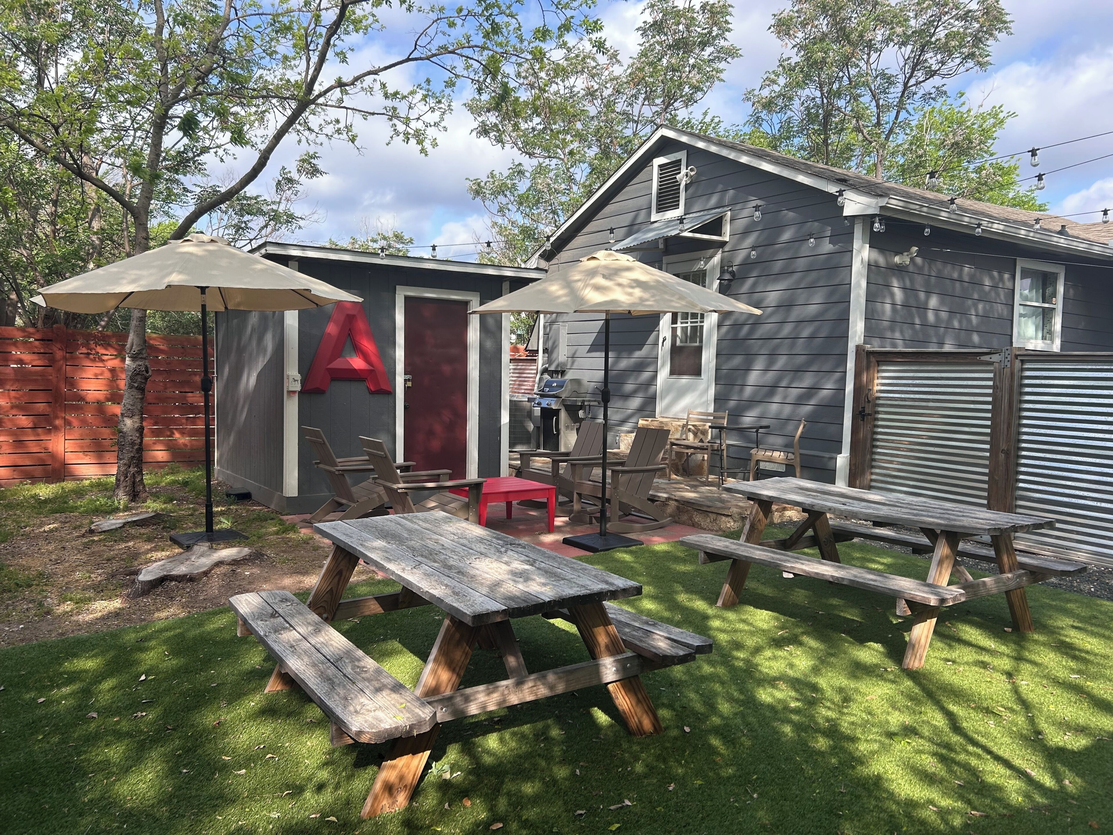 A backyard with a wooden deck, picnic tables, and a barbecue area.