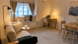 A cozy living room with a sofa, a small round table, a desk with a laptop, and a dining table with chairs. - Stony Stratford Cozy Apartment (Milton Keynes)