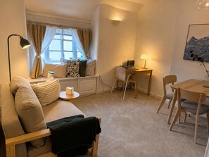 A cozy living room with a sofa, a small round table, a desk with a laptop, and a dining table with chairs. - Stony Stratford Cozy Apartment (Milton Keynes)