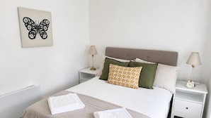 A neatly made bed with two pillows, a bedside lamp, and a wall art piece. - Stony Stratford Cozy Apartment (Milton Keynes)