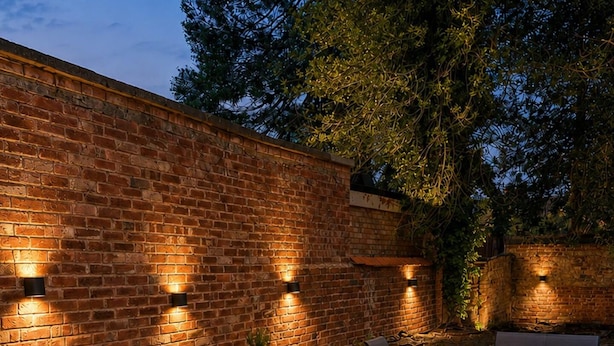 An outdoor patio area with brick walls, wicker furniture, and wall-mounted lighting. - Stony Stratford Cozy Apartment (Milton Keynes)