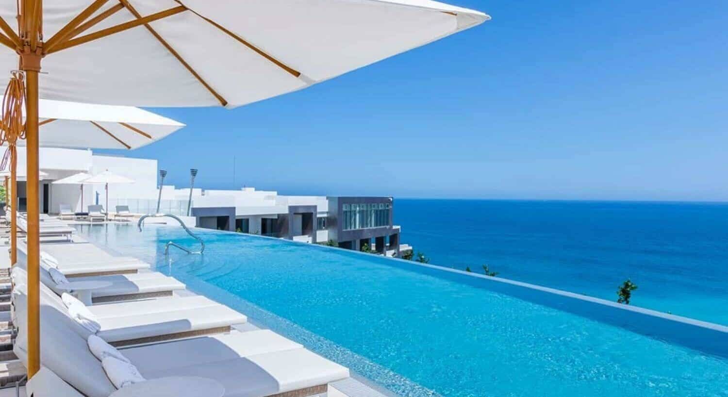 A poolside area with lounge chairs and umbrellas, overlooking a clear blue ocean.