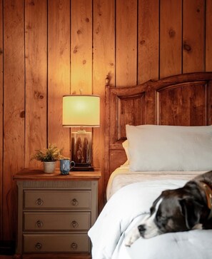 Eine Holzwand mit einem Nachttisch, einer Lampe, einer Pflanze und einem Bett, in dem ein Hund liegt.