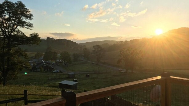 Ländliche Landschaft mit Sonnenuntergang, einem Holzzaun und einer entfernten Ansicht von Häusern und einer Straße.