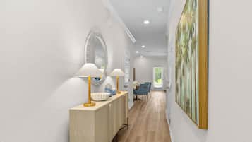 A hallway with a wooden console table, two lamps, a mirror, and a painting on the wall.