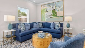 A living room with a blue sectional sofa, a round coffee table, two side tables with lamps, and a large abstract painting on the wall. - Bayside Getaway - Near Beach (Orange Beach)