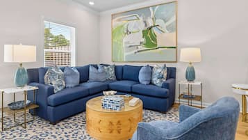 A living room with a blue sectional sofa, a round coffee table, two side tables with lamps, and a large abstract painting on the wall.
