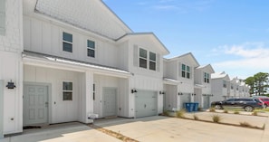 A row of white single-family homes with attached garages, a clear sky, and a parking area with cars. - Bayside Getaway - Near Beach (Orange Beach)