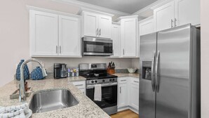 A modern kitchen with white cabinets, stainless steel appliances, a granite countertop, and a stainless steel sink. - Bayside Getaway - Near Beach (Orange Beach)