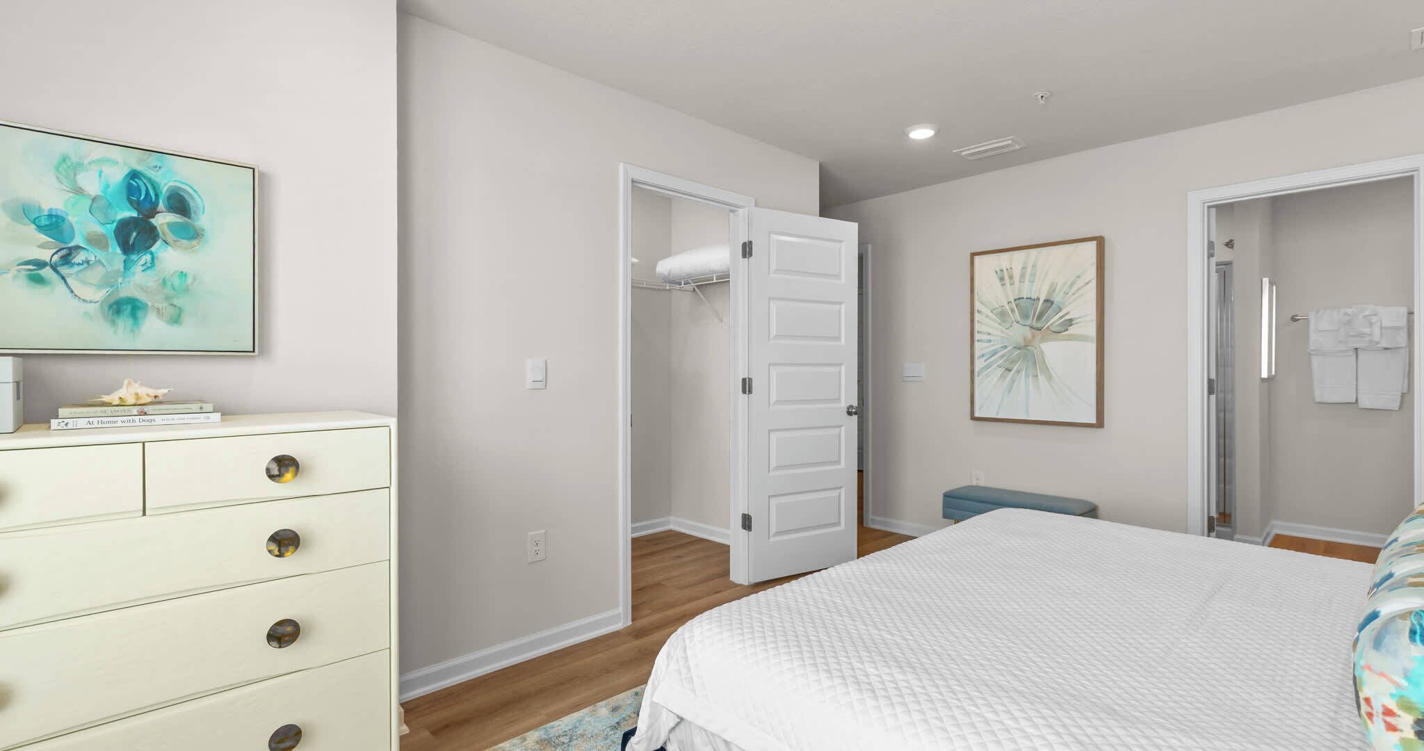 A bedroom with a bed, a dresser, a door leading to a bathroom, and a shower.