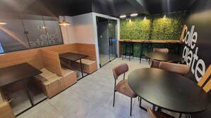 L’intérieur d’un café moderne, avec des sièges en bois, un bar et un mur végétal orné du nom du café.