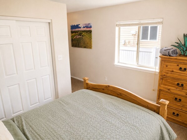 Un dormitorio con cama, cómoda, ventana y un cuadro colgado en la pared.