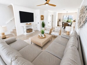 A modern living room with a large sofa, a coffee table, a TV, and a ceiling fan. - Gulf Winds East #12 - Pearl of the Sea (Miramar Beach)
