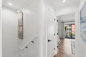 A hallway with white walls, a wooden floor, and a view to a balcony with a railing. - Gulf Winds East #12 - Pearl of the Sea (Miramar Beach)