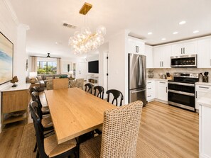 A modern kitchen with white cabinets, stainless steel appliances, and a dining area with a wooden table and wicker chairs. - Gulf Winds East #12 - Pearl of the Sea (Miramar Beach)