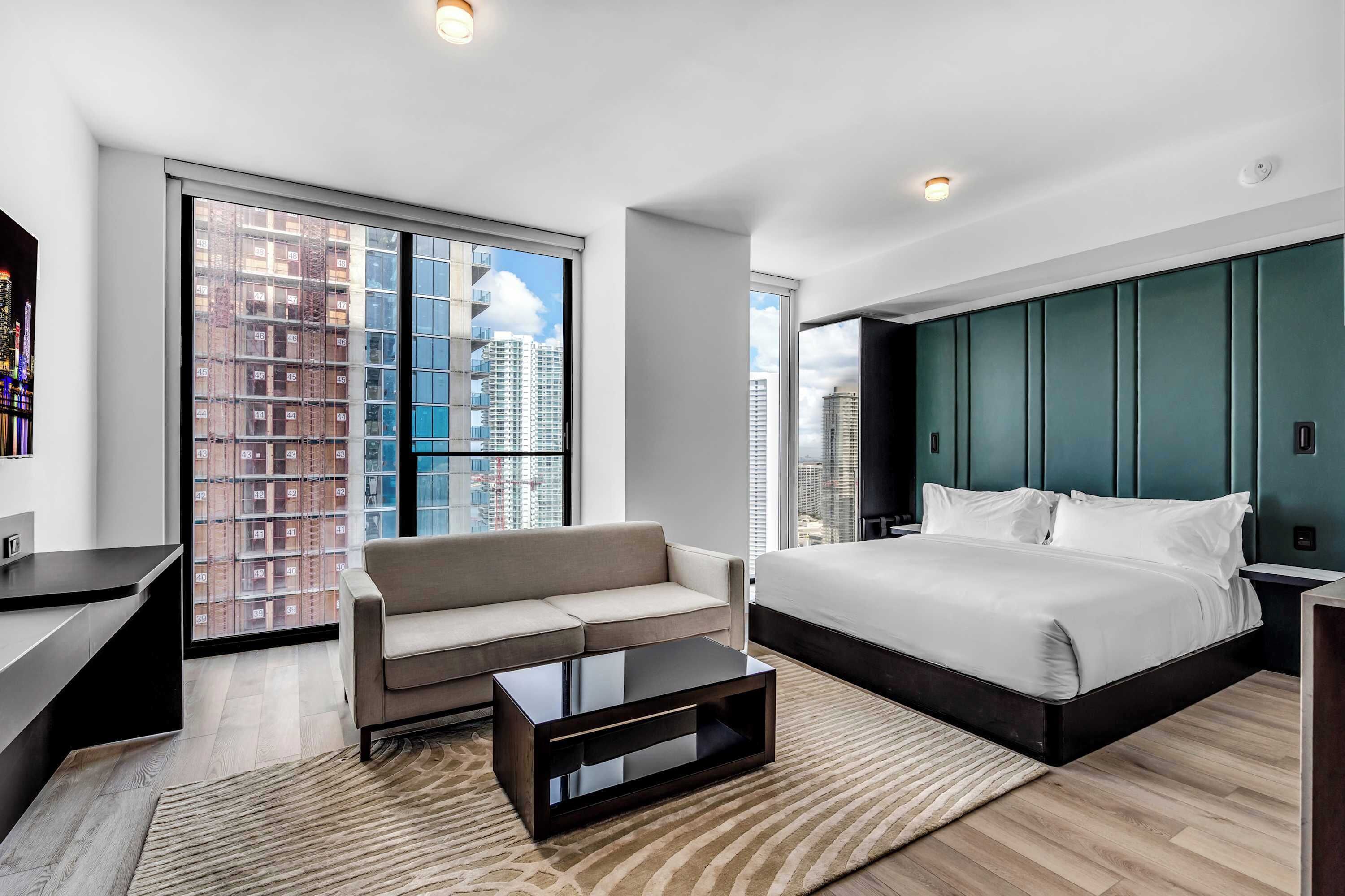 A modern hotel room with a large bed, a sofa, a coffee table, and a desk.