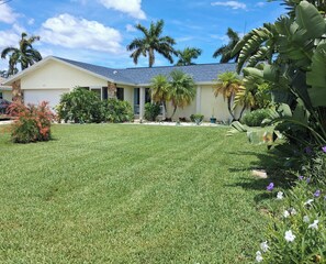 A residential house with a well-maintained lawn, palm trees, and various shrubs. - Cape Coral Waterfront BOAT HOUSE ! gulf access 3-bedroom house , pet friendly. (Cape Coral)