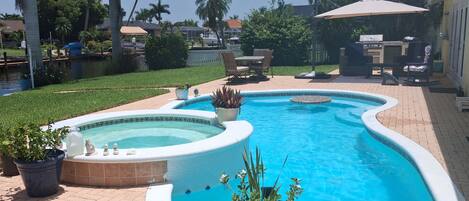 A swimming pool with a hot tub, surrounded by potted plants and outdoor furniture.