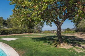 A tree-lined yard with a swimming pool, a clear sky, and distant hills. - Luxury Escape, Backyard Pool & Hillside Views (Los Angeles)