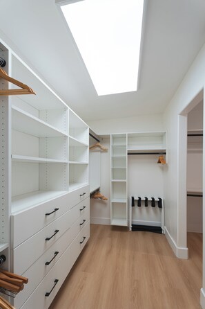 Ein begehbarer Kleiderschrank mit offenen Regalen, Platz zum Aufhängen von Kleidung und einem Oberlicht.