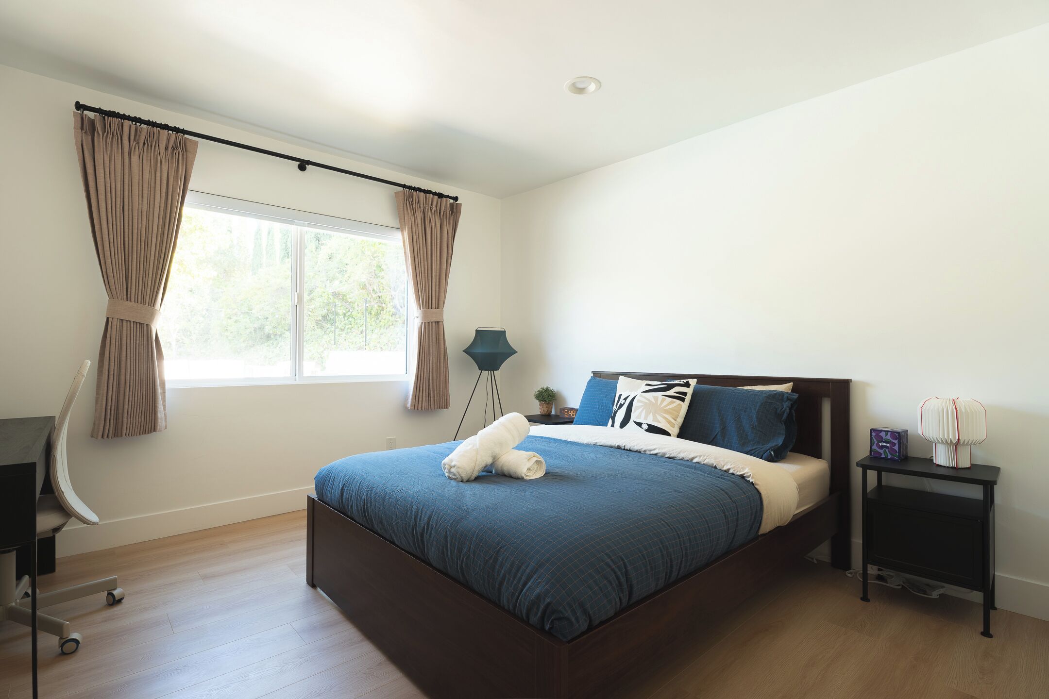 Ein Schlafzimmer mit einem Bett, einem Schreibtisch, einem Stuhl, einem Nachttisch und einem Fenster mit Vorhängen.
