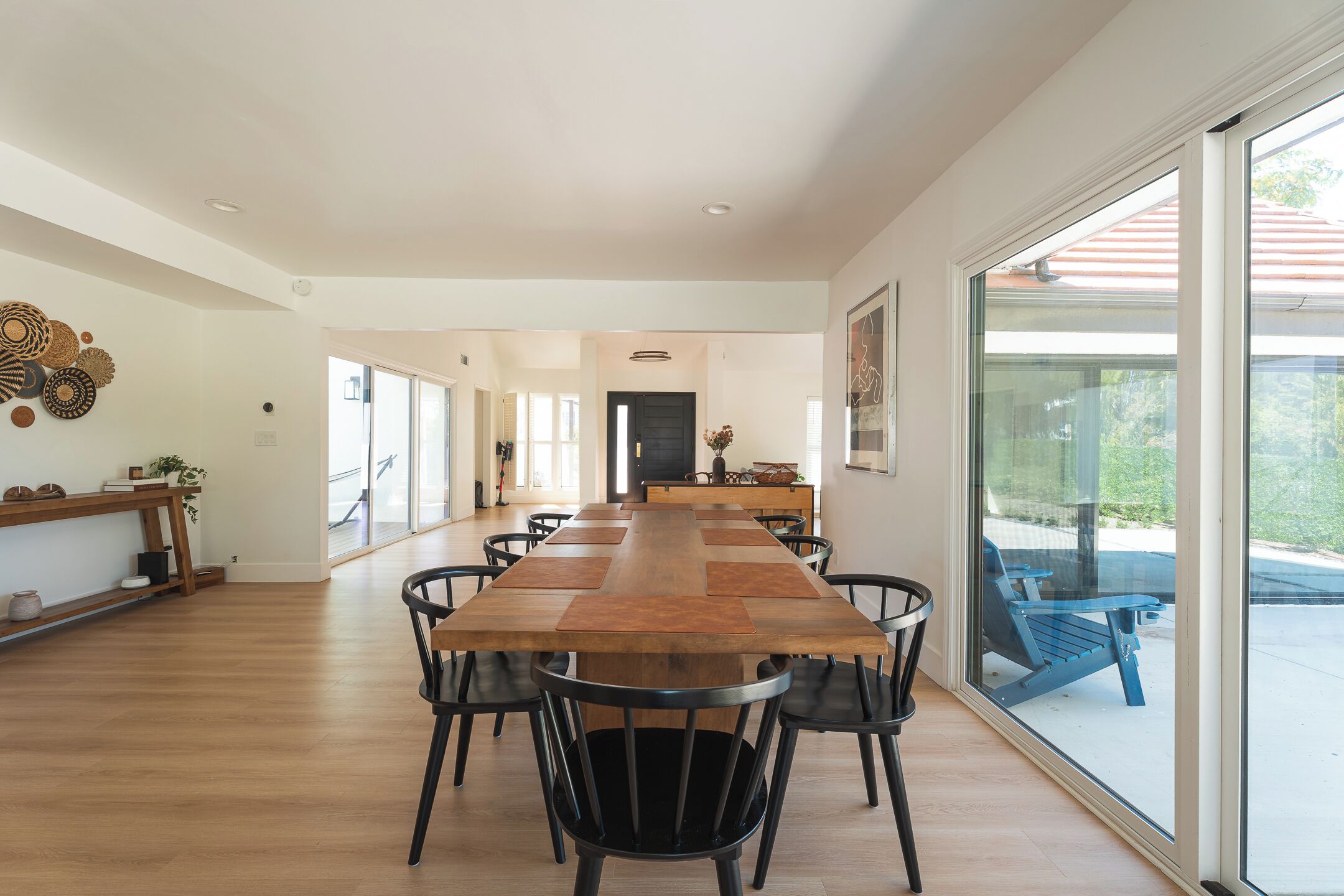 Een ruime eethoek met een lange houten tafel, zwarte stoelen en uitzicht door grote glazen deuren.