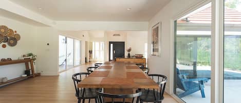 A spacious dining area with a long wooden table, black chairs, and a view through large glass doors.