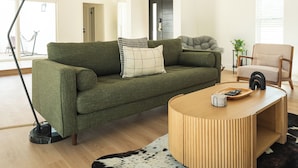 A modern living room with a green sofa, a round wooden coffee table, a black floor lamp, and a cowhide rug. - Luxury Escape, Backyard Pool & Hillside Views (Los Angeles)