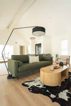Ein modernes Wohnzimmer mit einem grünen Sofa, einem runden Couchtisch aus Holz, einer schwarzen Stehlampe und einem Kuhfellteppich.