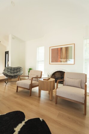 Ein modernes Wohnzimmer mit Kamin, Holzboden und einer Sitzecke mit Sofa und Sesseln.