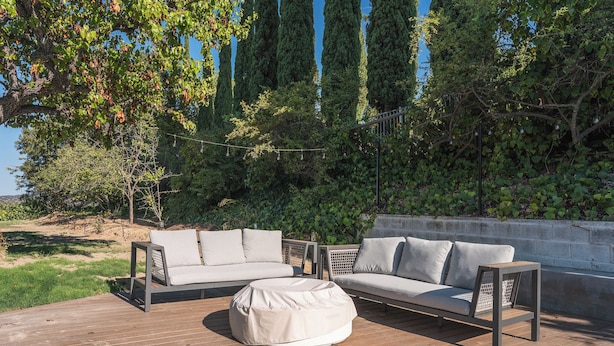 An outdoor deck with a sofa, ottoman, and table, surrounded by greenery and trees. - Luxury Escape, Backyard Pool & Hillside Views (Los Angeles)