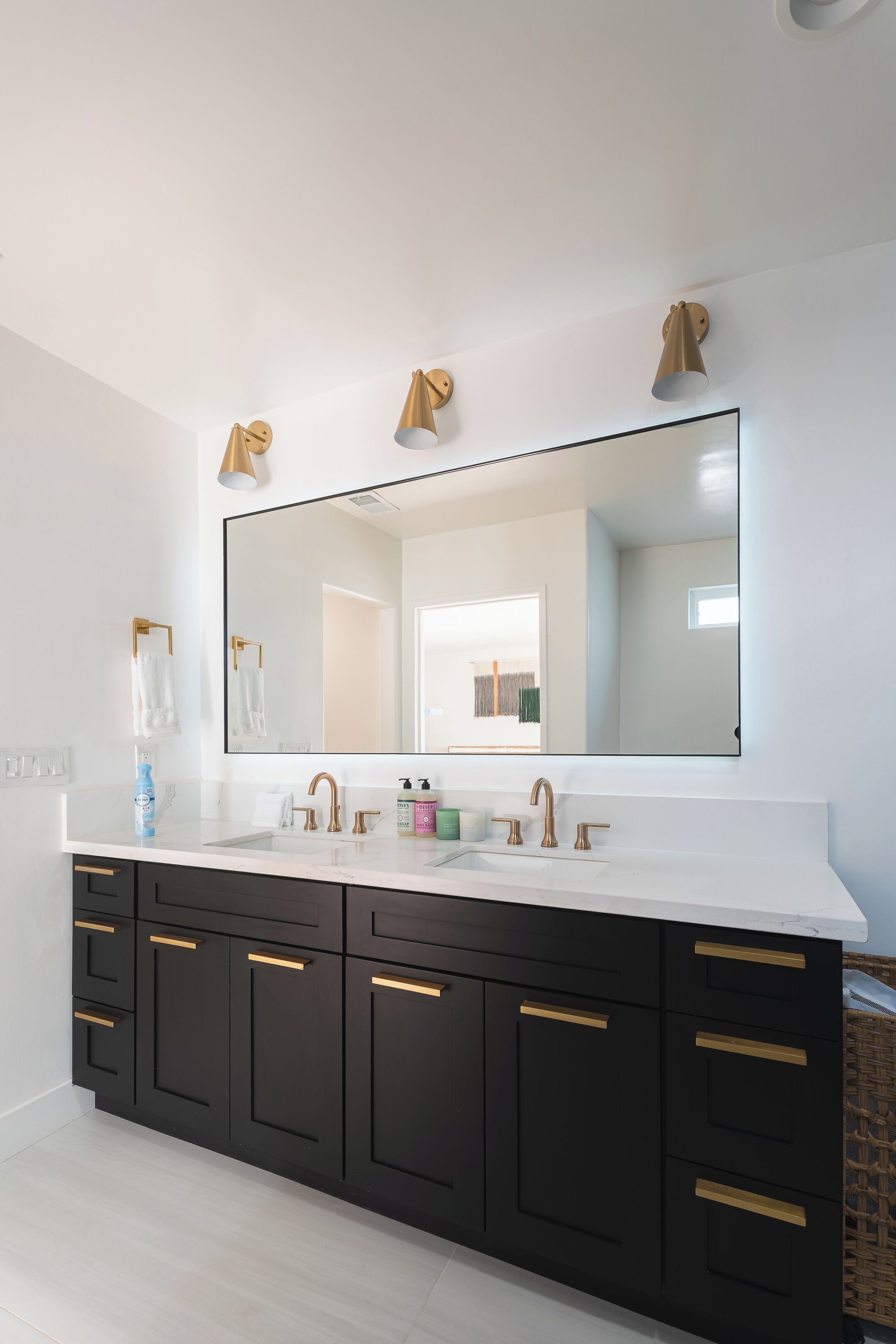 Un baño moderno con un espejo grande, una encimera blanca y armarios negros con detalles dorados.
