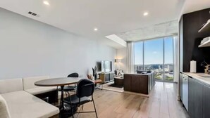 A modern apartment with a dining area, a kitchen, and a large window offering a city view. - Luxury High-Rise 2BR (Austin)
