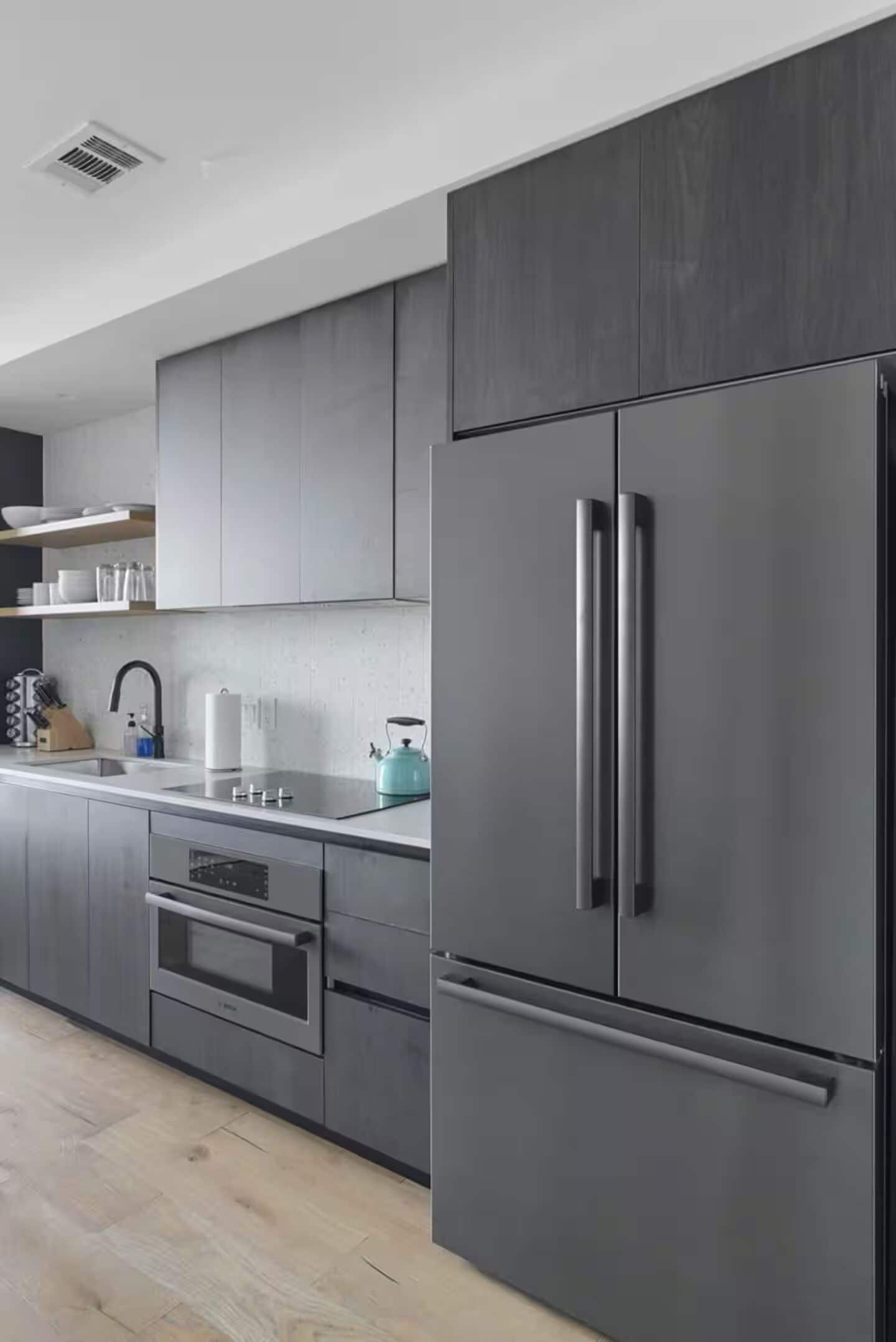 Une cuisine moderne avec des meubles de couleur grise, un réfrigérateur en acier inoxydable et un four encastré.