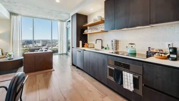 A modern kitchen with dark cabinetry, a large window, and a view of the city. - Luxury High-Rise 2BR (Austin)