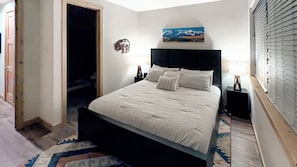 Ein Schlafzimmer mit einem Bett, einem Nachttisch, einer Lampe, einem Bild an der Wand und einer Tür zu einem anderen Raum.