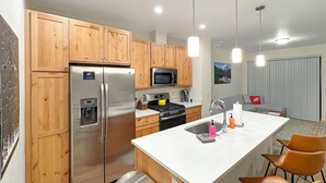 Uma cozinha moderna com armários de madeira, eletrodomésticos de aço inoxidável, uma ilha central com banquetas e iluminação pendente.