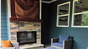 A covered outdoor seating area with wicker furniture, a stone fireplace, and a ceiling fan. - Escape to a peaceful retreat with breathtaking golf course views in Helen.  (Helen)