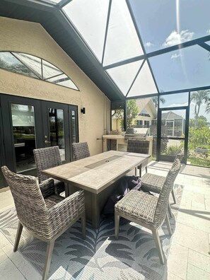 A covered patio with a table and chairs, a grill, and a view of the surrounding area. - Villa Van Vista Luxury Gulf Access Retreat (Cape Coral)